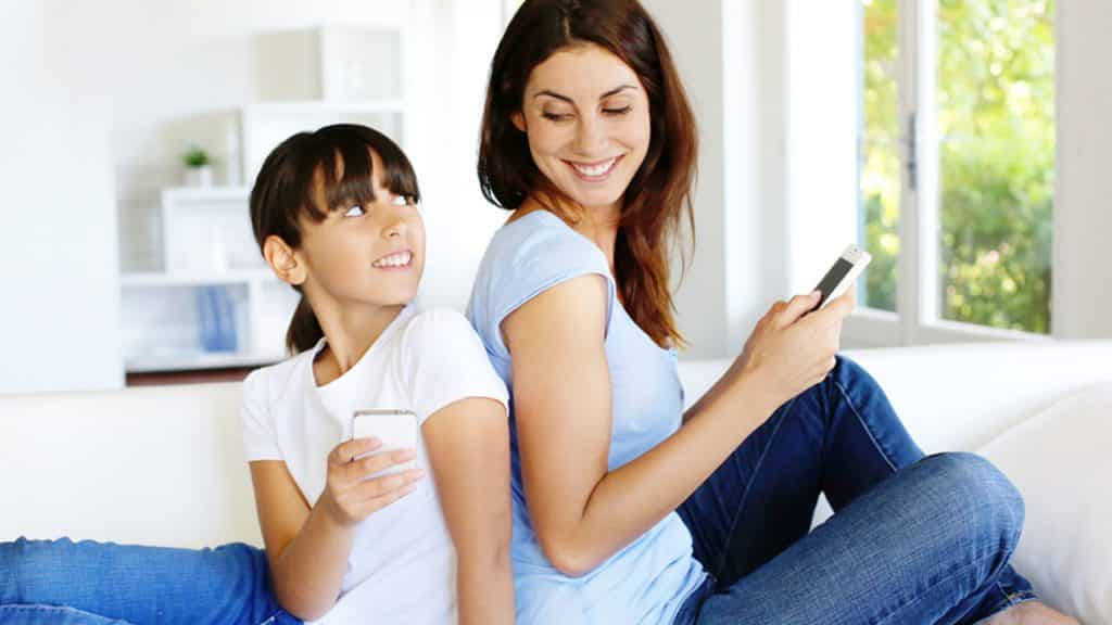 Mulher e menina sentadas no sofá, sorrindo, olhando o celular