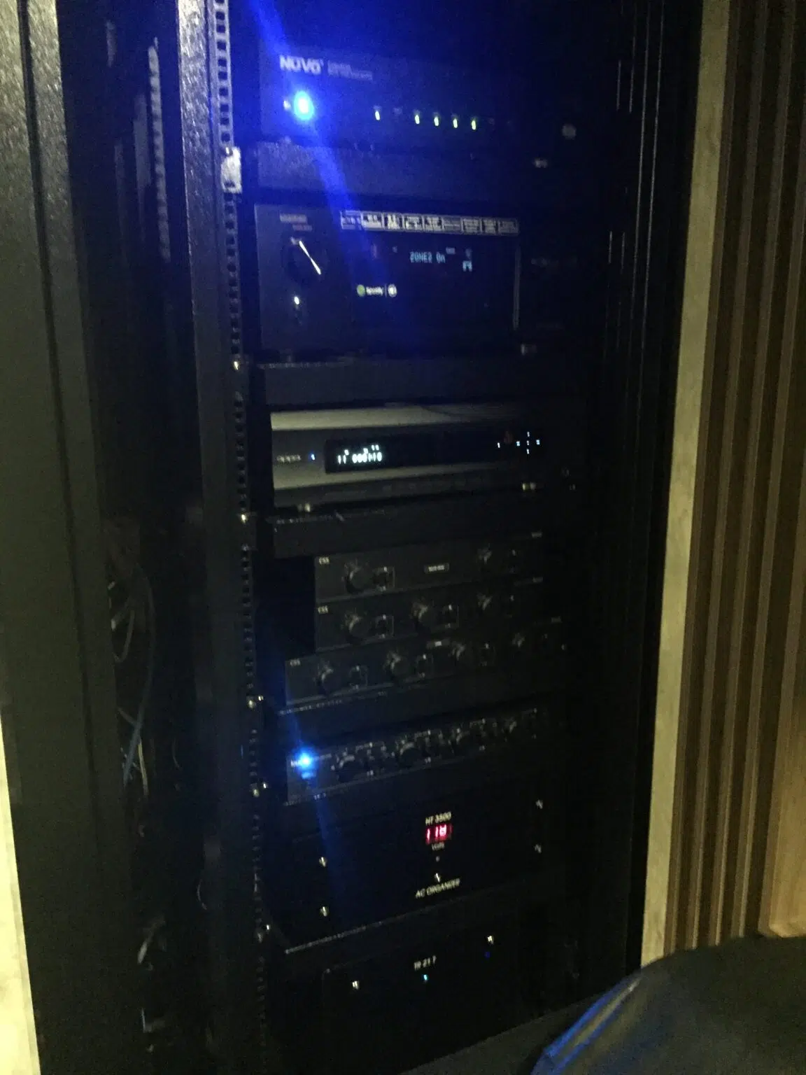 Rack de equipamentos de áudio e vídeo montado num nicho de marcenaria, com as luzes dos aparelhos acesas