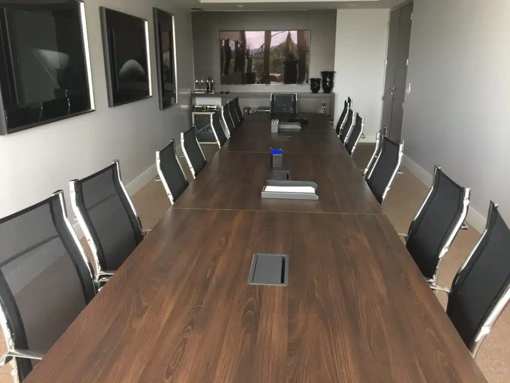 Sala de reuniões com mesa longa de madeira, cadeiras pretas e TVs nas paredes laterais, projeto da Starvai