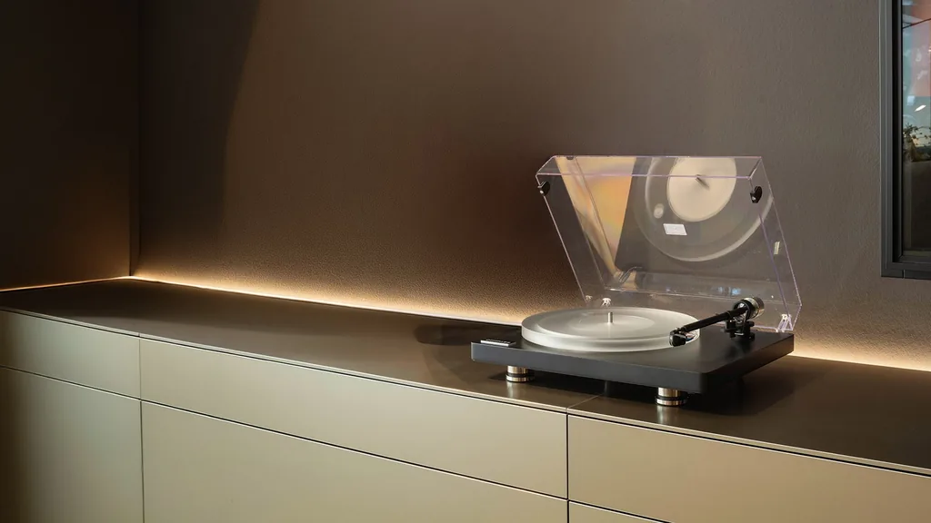 Toca-discos Clearaudio Compass com tampa de acrílico aberta, sobre aparador com iluminação indireta numa sala de estar