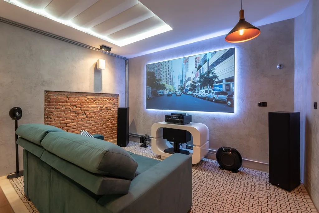 Sala de home cinema com sofá, caixas acústicas e tela de projeção Dual Screen iluminada por LED na parede de cimento queimado