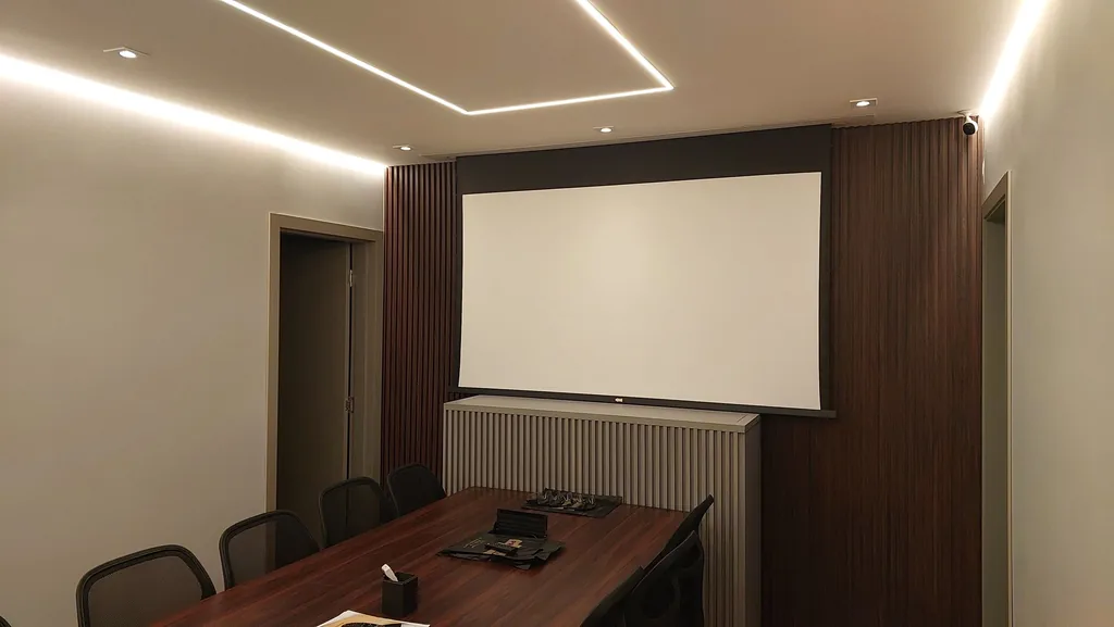 Sala de reunião do showroom Projetelas com tela de projeção motorizada embutida no forro, entre painéis de madeira ripada